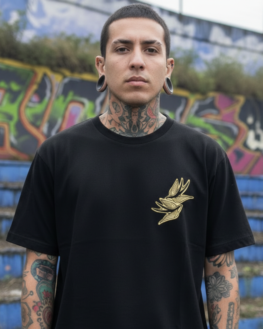 Modelo con tatuajes usando camiseta negra Tattoo Roots de corte relajado. Streetwear colombiano de autor con diseño de golondrina neotradicional en el pecho.