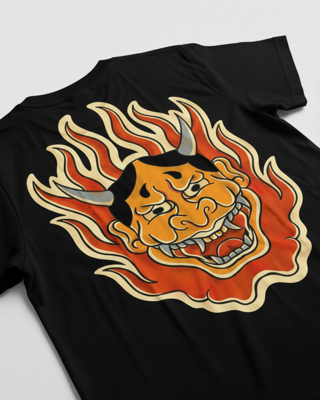 Diseño de espalda completa en camiseta negra: Máscara Hannya japonesa rodeada de llamas naranjas y amarillas. Arte original de tatuadores colombianos para TatuRoots, estilo streetwear de autor