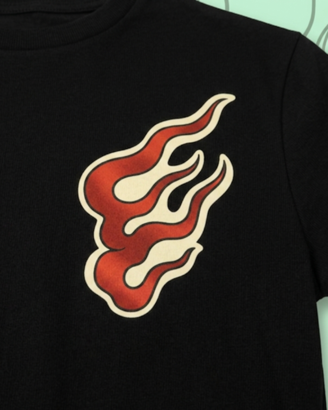 Primer plano de camiseta negra Tattoo Roots con diseño de llama estilo tatuaje tradicional en el pecho. Colores rojo y crema con bordes definidos sobre tela de algodón de alta calidad.