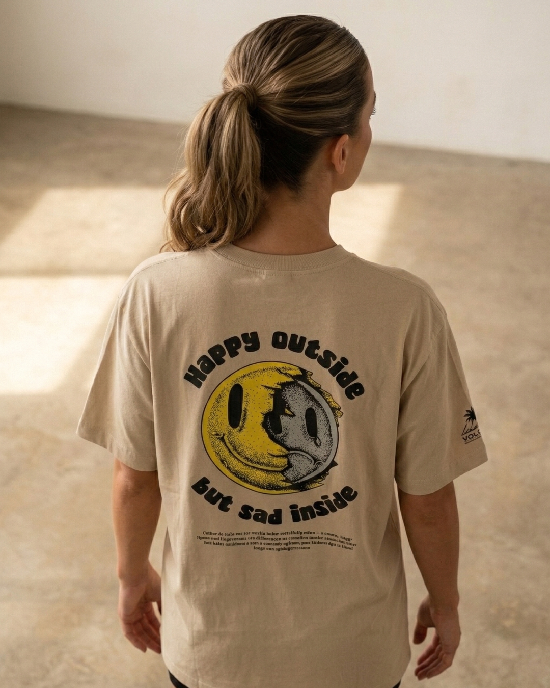 modelo mujer con Camiseta streetwear beige Grin & Grit de Tattoo Roots, diseño de tatuador Motley con cara fragmentada en la espalda.
