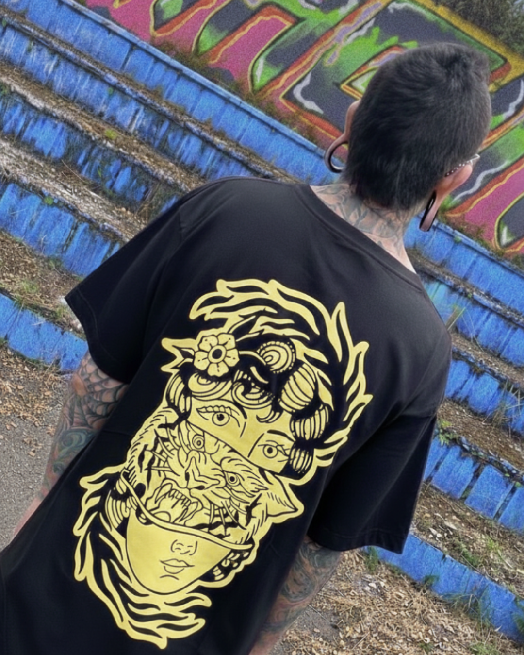 Vista posterior de camiseta Tattoo Roots en exteriores: ilustración neotradicional de mujer y tigre en color crema sobre textil negro. Estética streetwear de autor inspirada en el tatuaje.