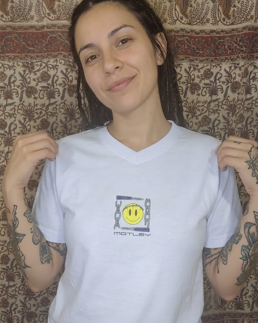 Modelo mujer con tatuajes y rastas luciendo el frente de la camiseta Motley Smiley Core. Streetwear de autor con diseño de carita y corona de espinas. Estética urbana y artística de Tattoo Roots Colombia.